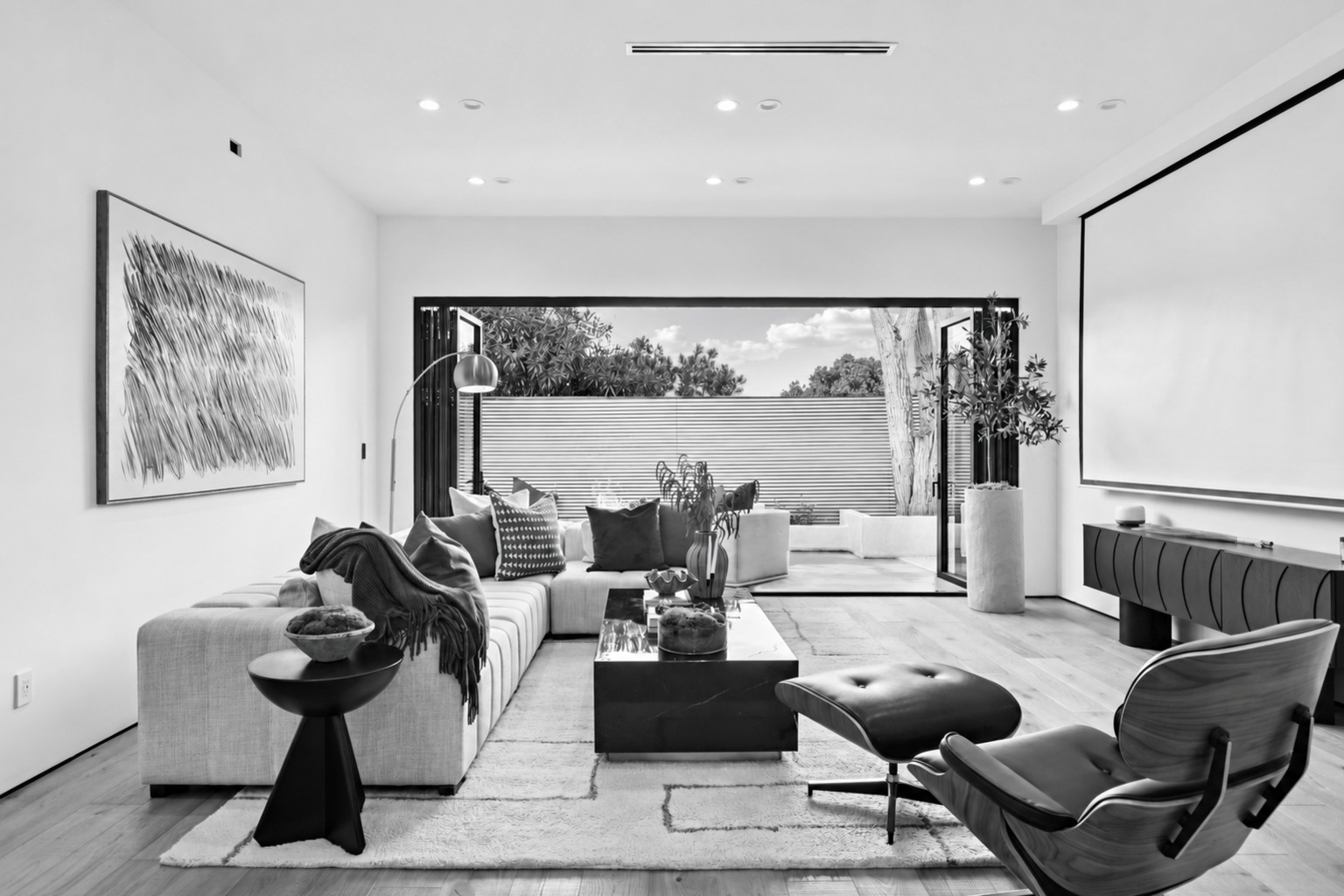 Black-and-white view of The Light House living room with an Eames lounge chair and a full-width opening to the courtyard